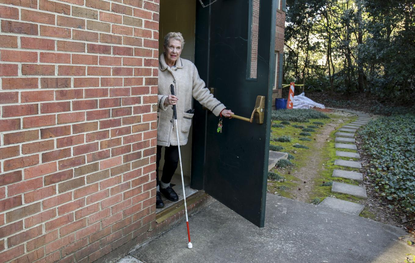 low vision woman steps out of building with a white cane