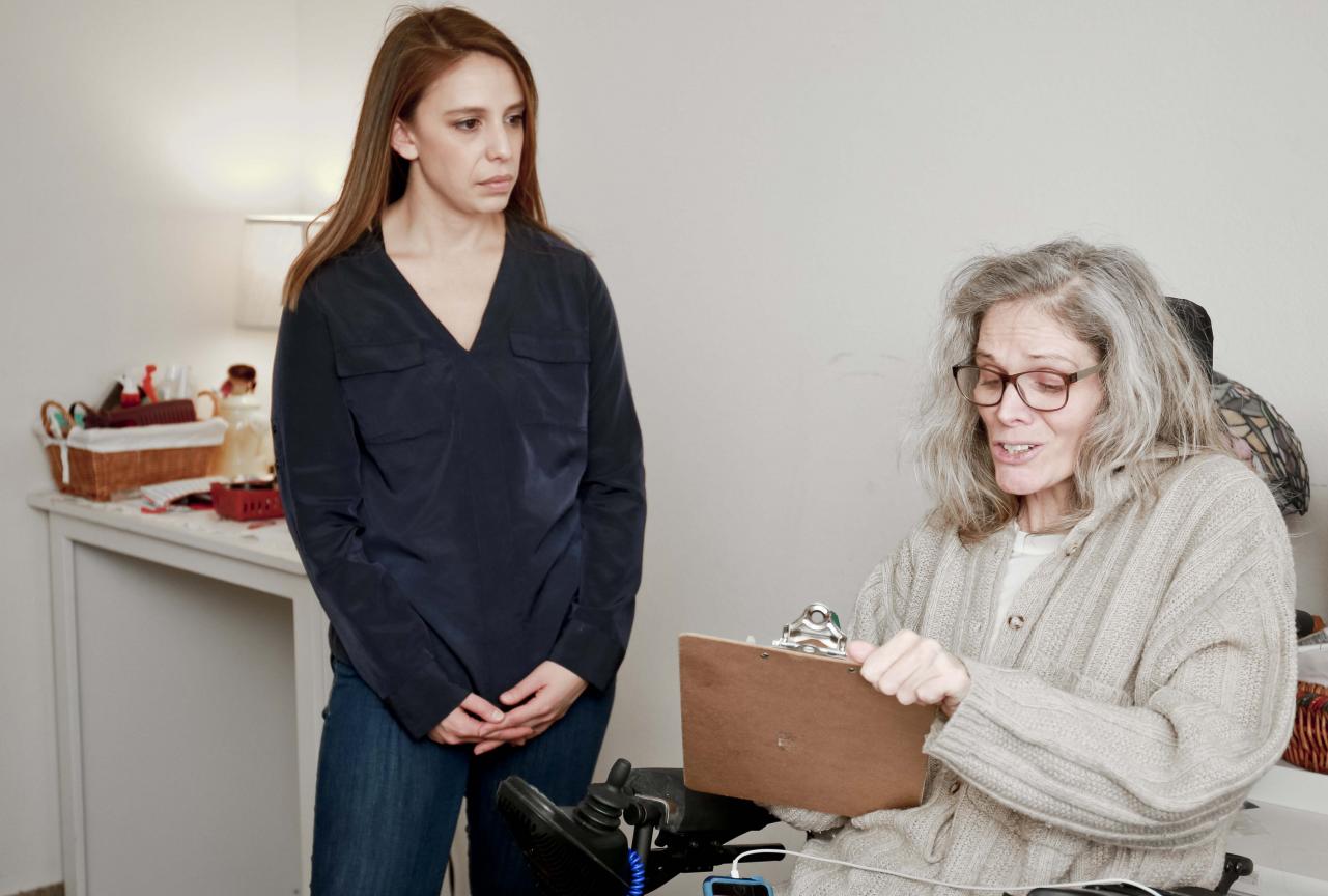 Woman in a wheelchair filling out a form with a woman standing next to her
