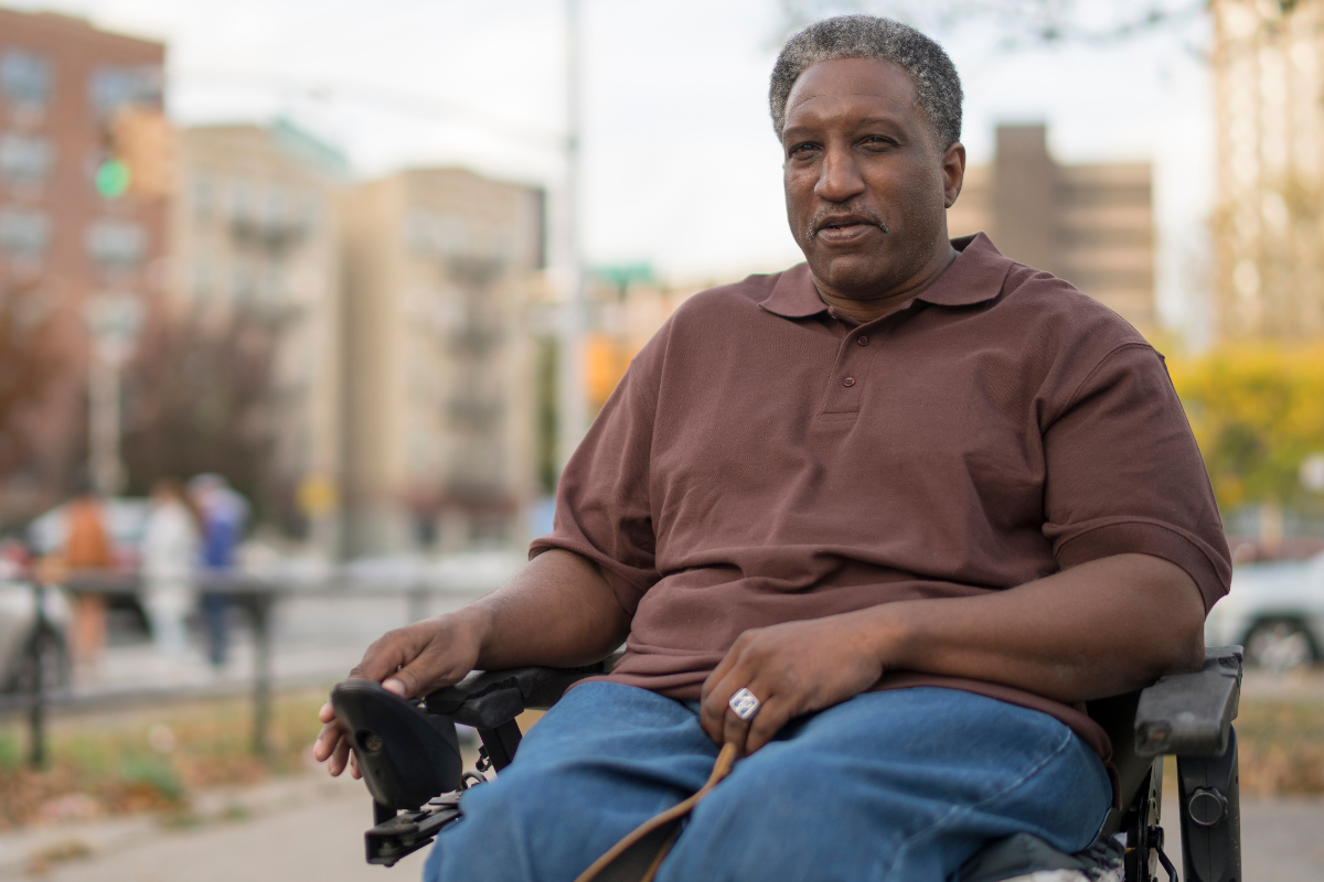 An older black man and veteran seated in a wheelchair outdoors on the street in the Bronx, New York City, USA.