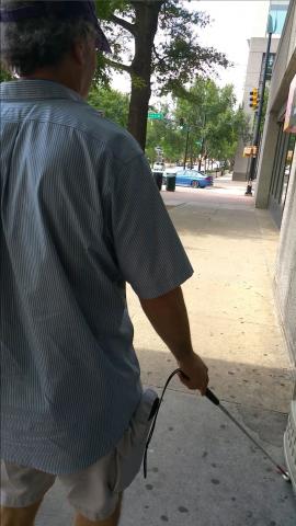 Man walking on sidewalk using a white cane to navigate