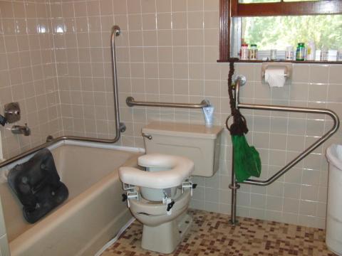 Bathroom with several accessibility modifications including grab bars along the toilet and bathtub and a raised toilet seat